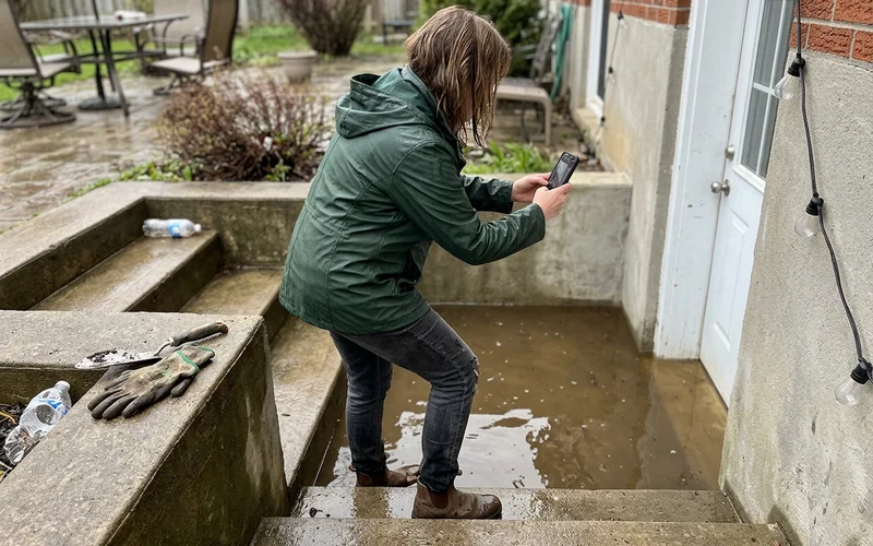 Homeowner photographing a flooded walkout landing with a phone