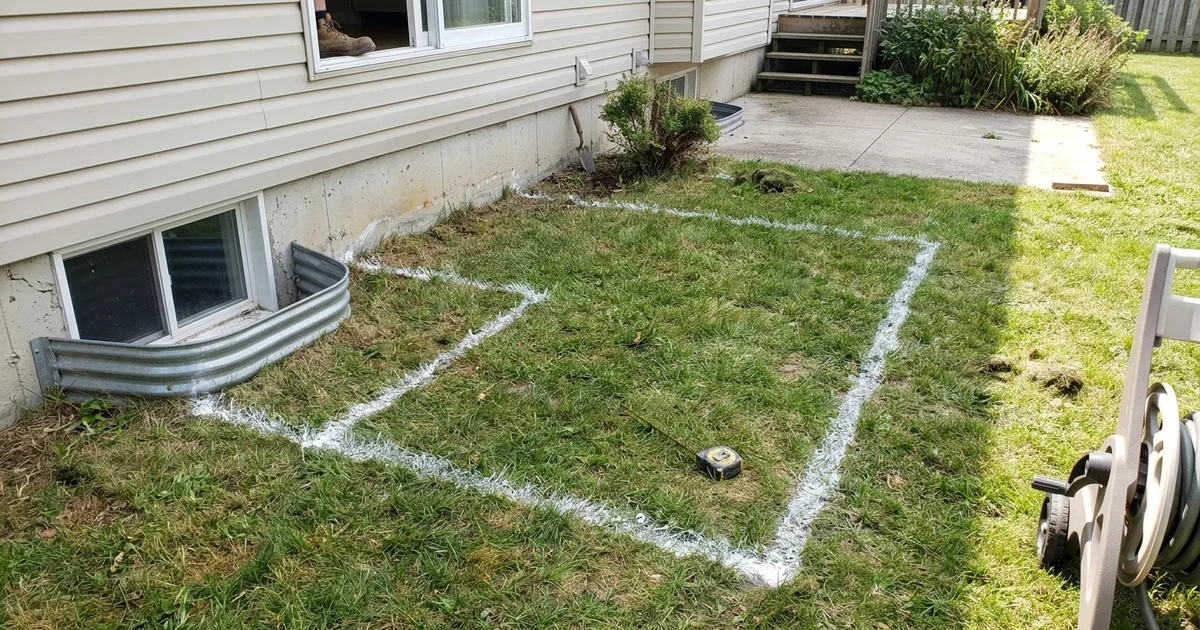 Basement window well beside a foundation where a walkout door is planned